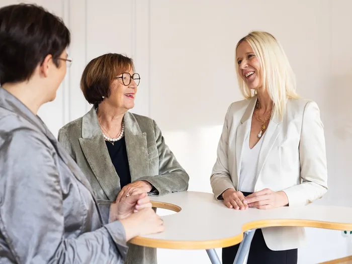 Drei Frauen im Gespräch am Stehtisch: Mitarbeitergespräche üben in der Weiterbildung Systemisch Führen