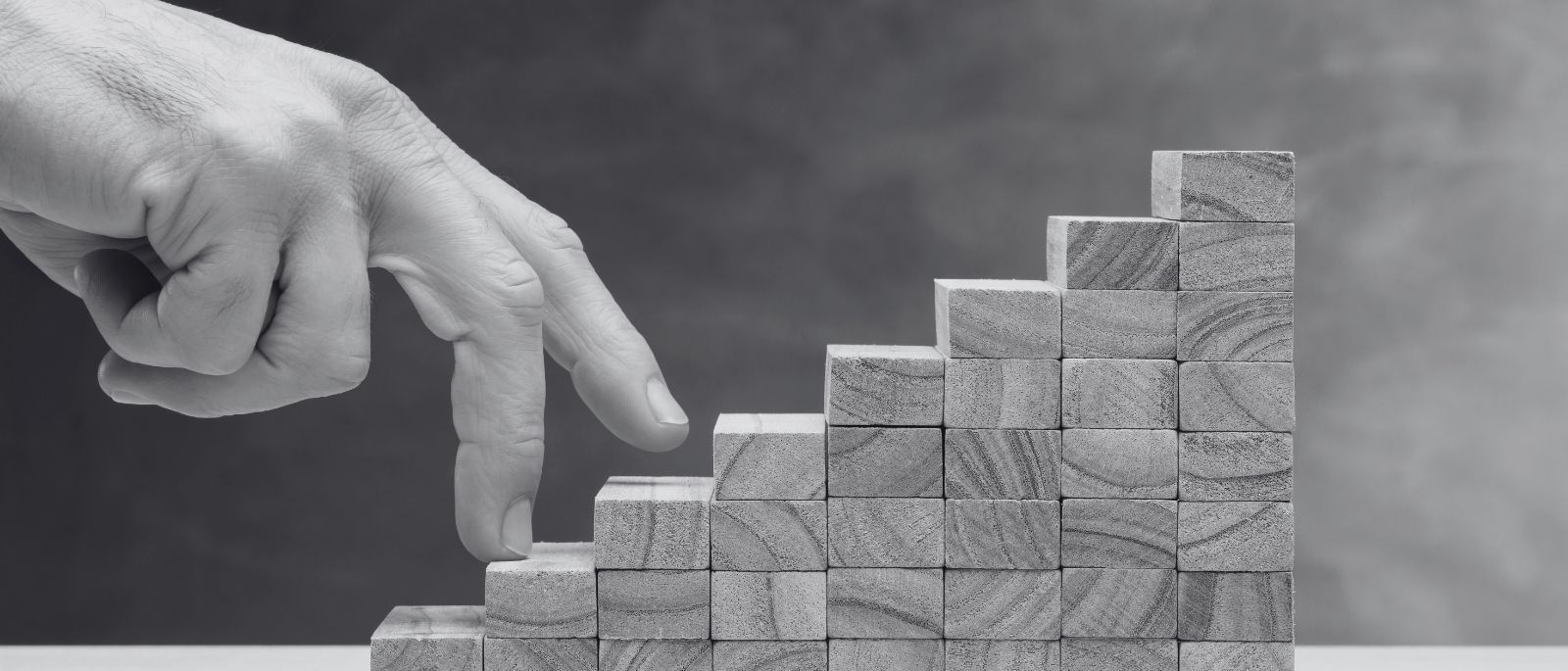Hand steigt symbolisch eine Treppe aus Holzblöcken hinauf – Sinnbild für Entwicklung und Wachstum